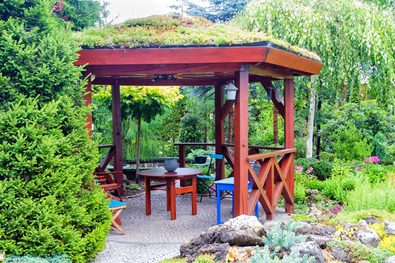 Wooden gazebo in a lush garden with tables, chairs, and colorful flowers