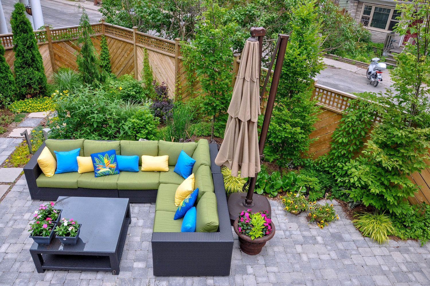 Outdoor patio with gray sectional, bright cushions, umbrella, and potted plants on a stone terrace