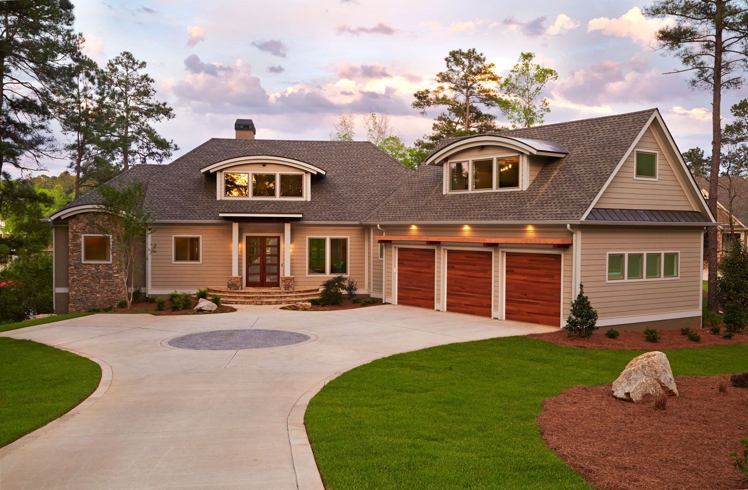 Large suburban house with a curved driveway, red garage doors, and landscaped lawn at dusk