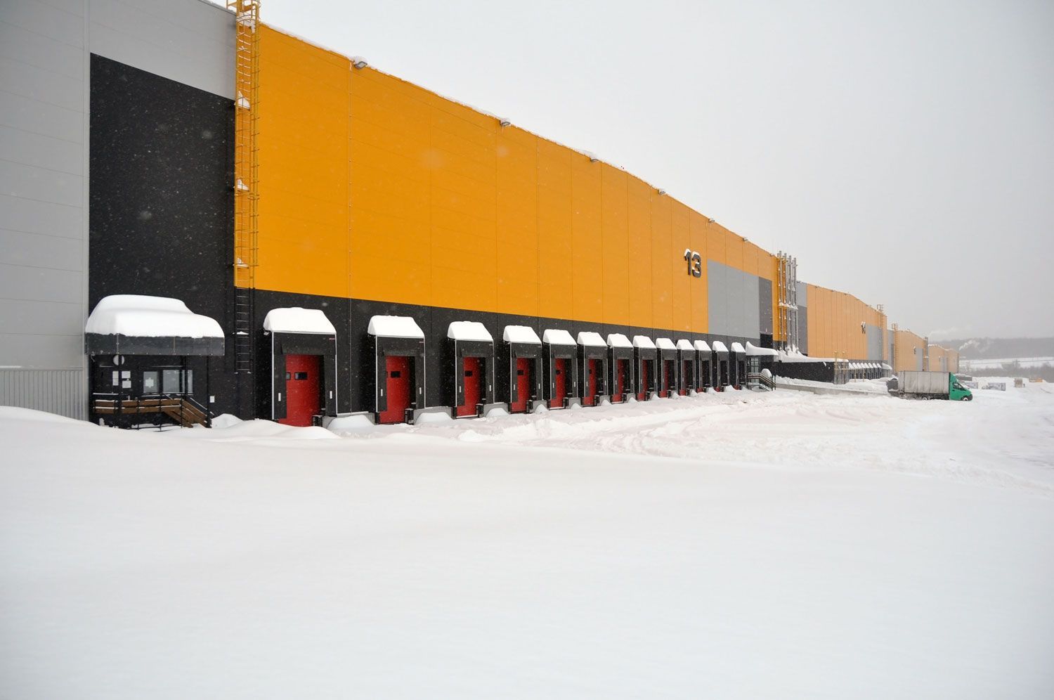 Snow-covered industrial building with a long orange and black facade and loading docks