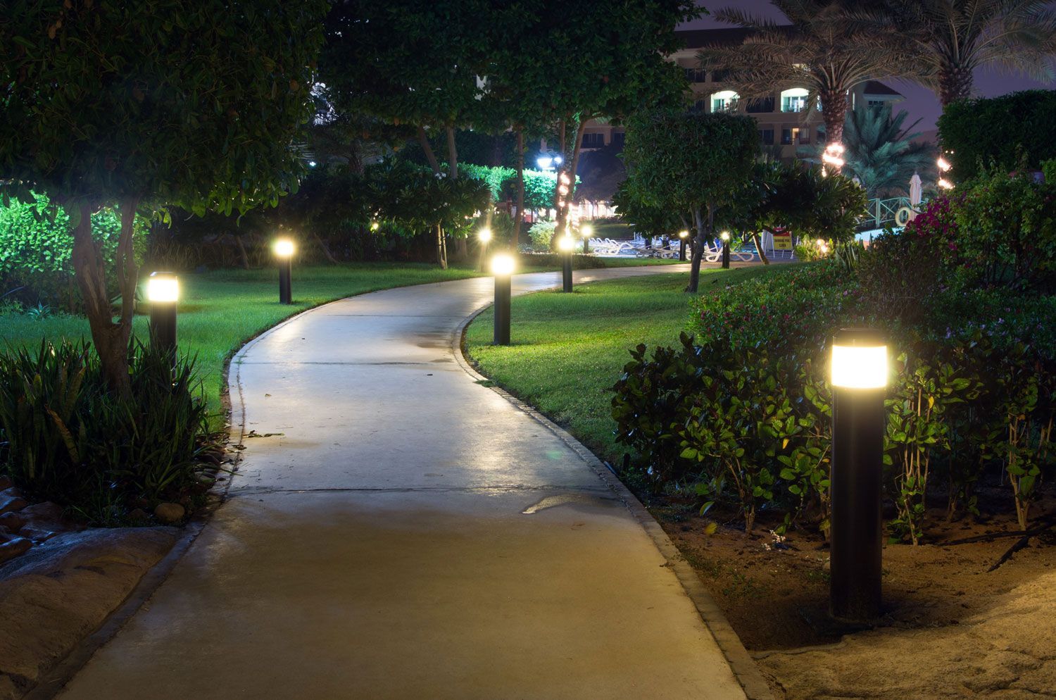 Illuminated winding walkway through a landscaped garden at night, with glowing path lights and bushes