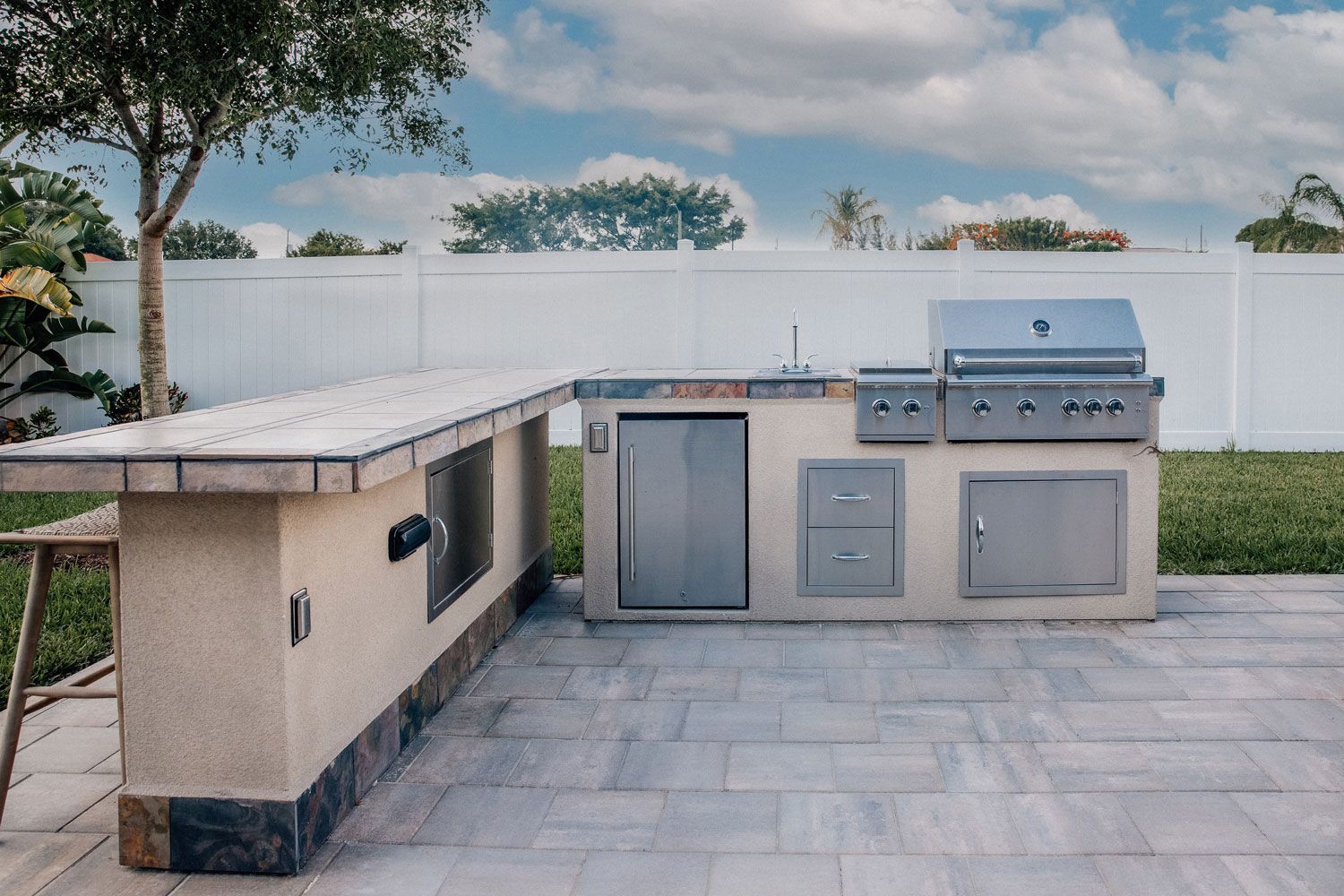 Outdoor stone kitchen and barbecue area with built-in grill, cabinets, and counter beside a patio wall