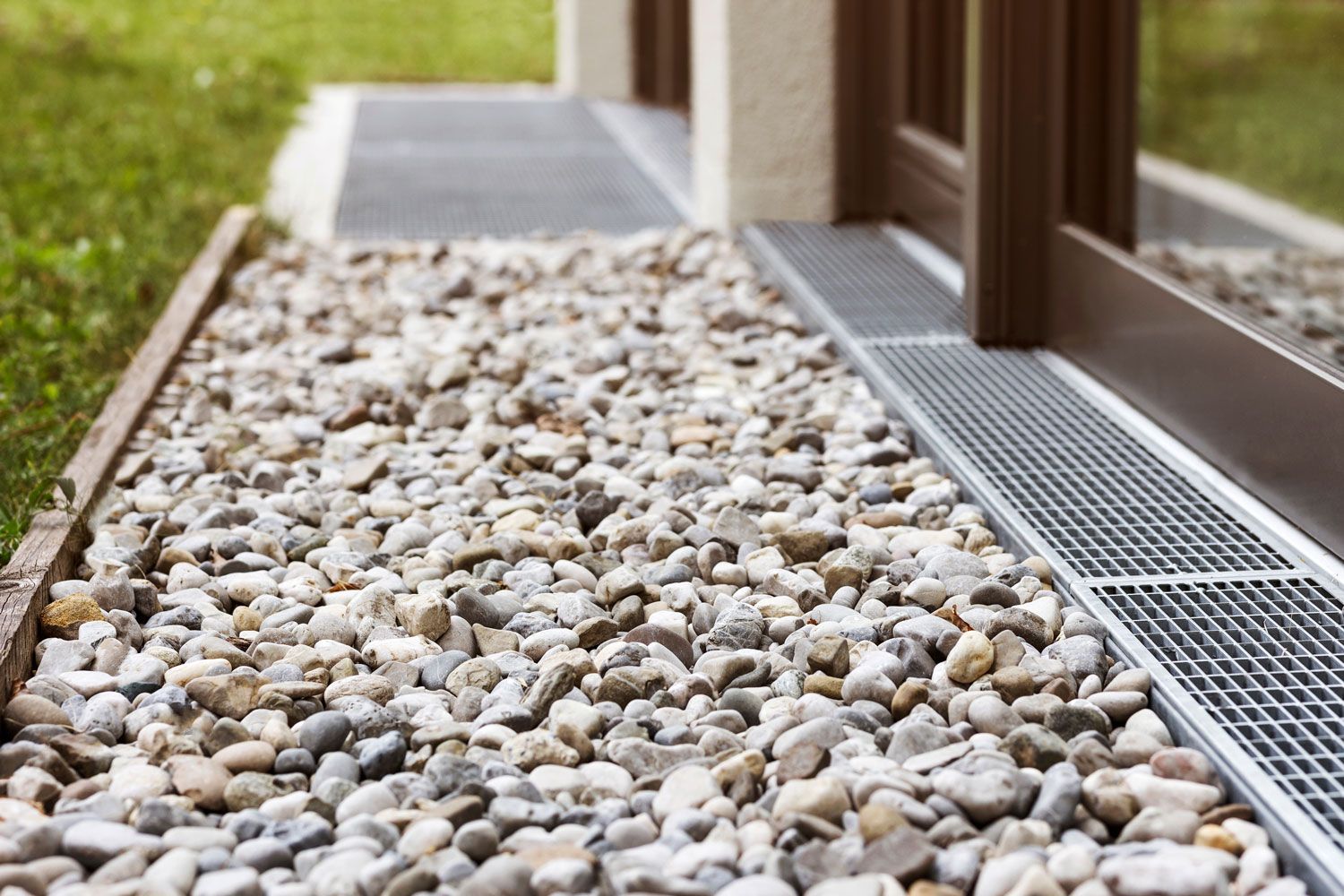Gravel landscaping beside a modern deck with a metal drainage grate and wooden post
