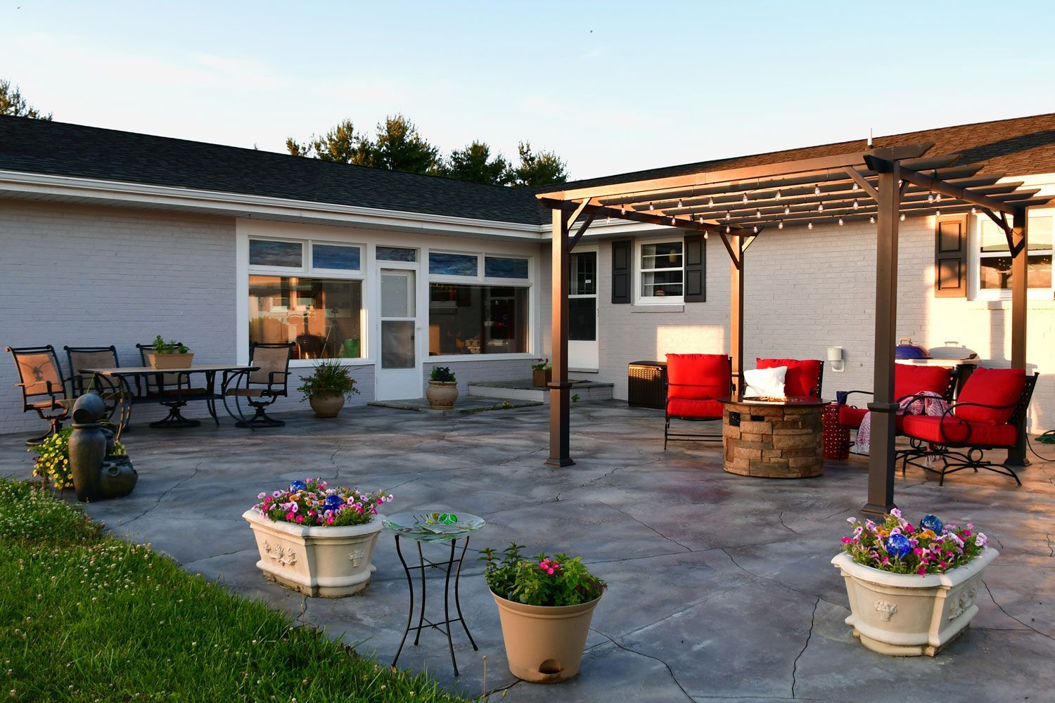 Patio with red chairs, potted flowers, and a pergola beside a white house