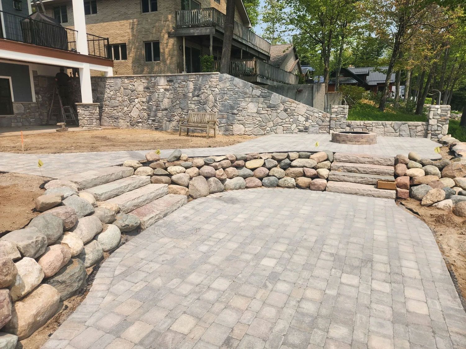 Stone-lined paved courtyard beside a rustic building and trees