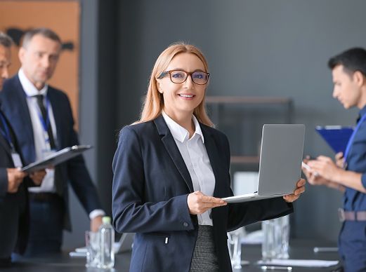 Business meeting with a woman holding a laptop, with two colleagues in the background.