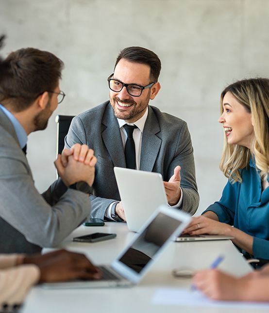 Colleagues in a meeting, smiling and discussing around a laptop in a bright office.