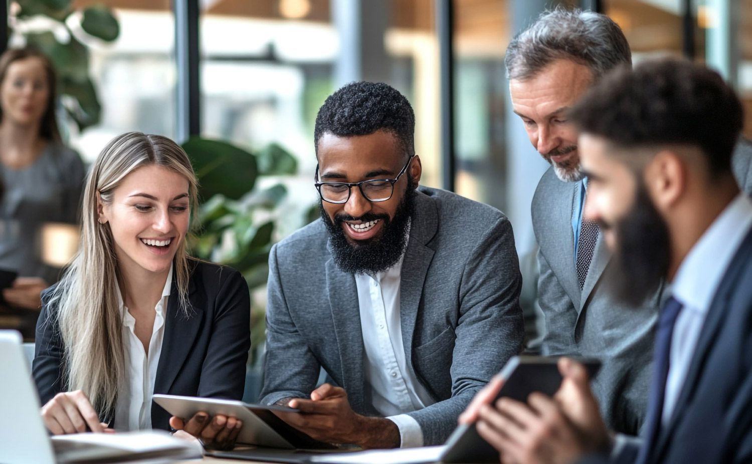 Coworkers smiling and discussing a tablet in a bright office meeting