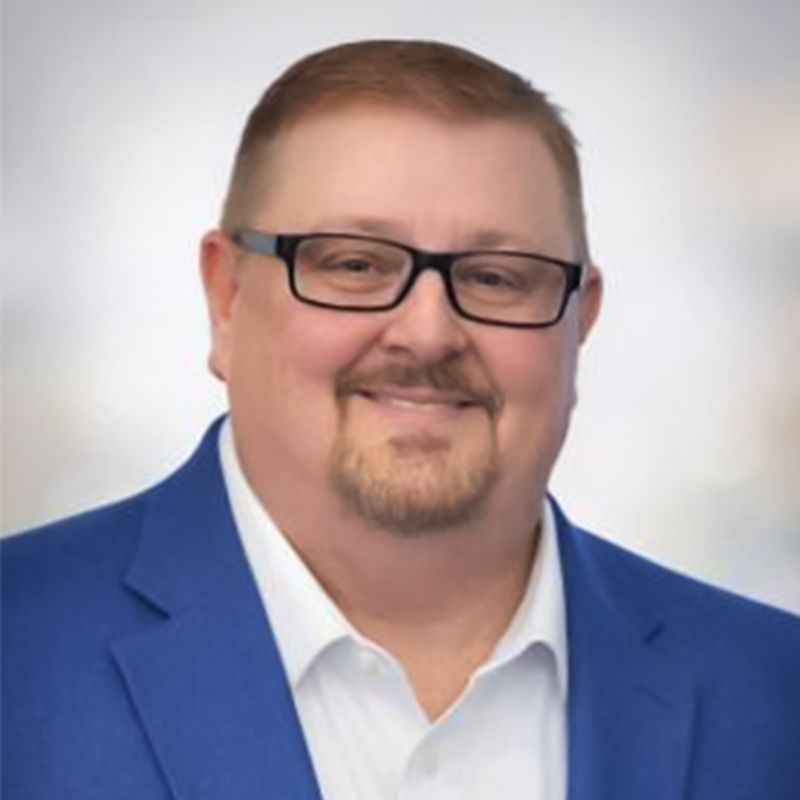 Smiling man in glasses wearing a blue blazer and white shirt against a light background