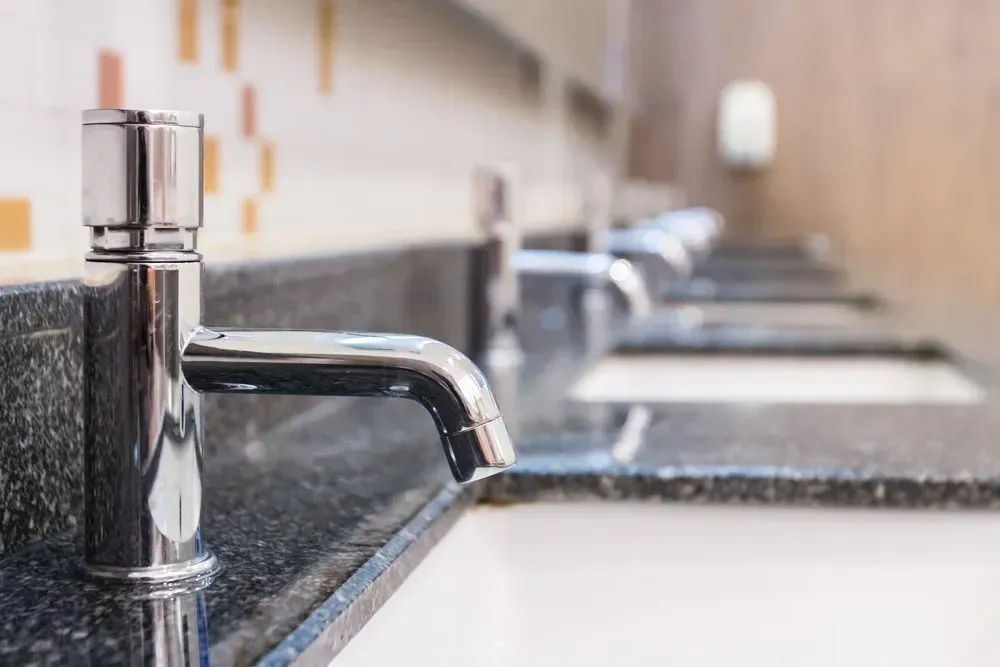 Row of Faucets on a Dark Granite Countertop in a Bathroom — Gibson Plumbing & Roofing Pty Ltd in Gladstone Central, QLD
