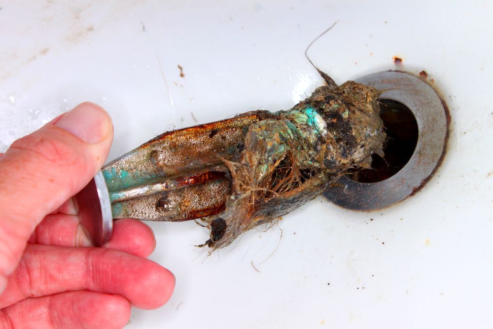 Hand Holding a Rusted Sink Stopper Covered in Hair and Debris — Gibson Plumbing & Roofing Pty Ltd in Gladstone, QLD