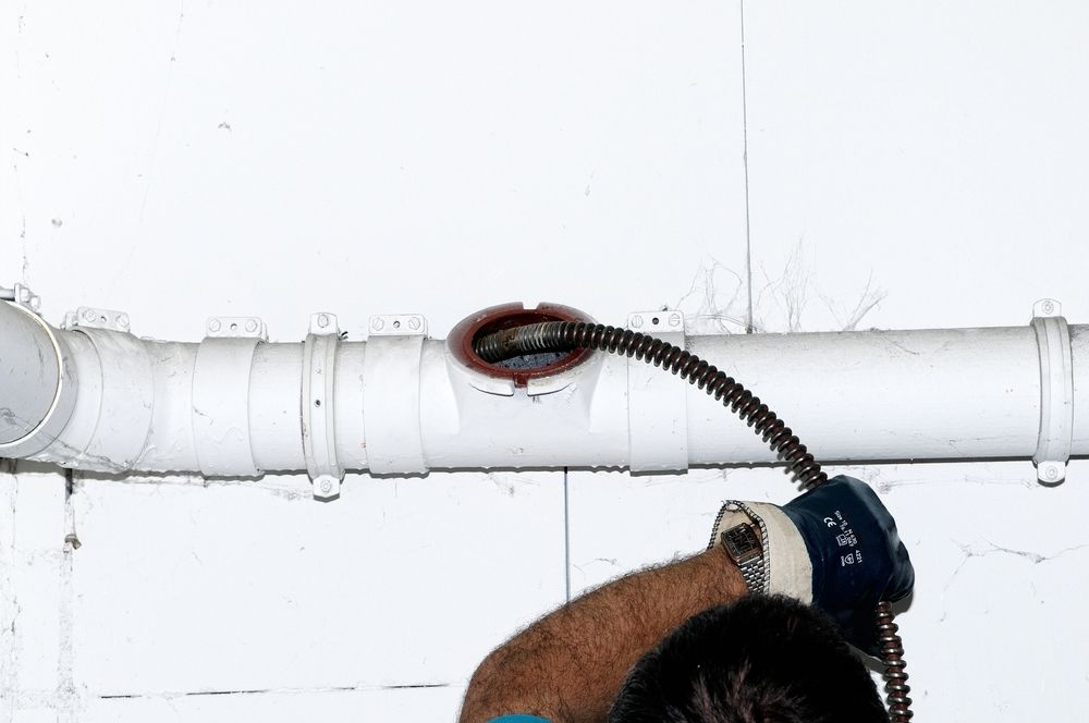 A Person Using a Plumbing Snake to Unclog a White Pipe — Gibson Plumbing & Roofing Pty Ltd in Gladstone, QLD