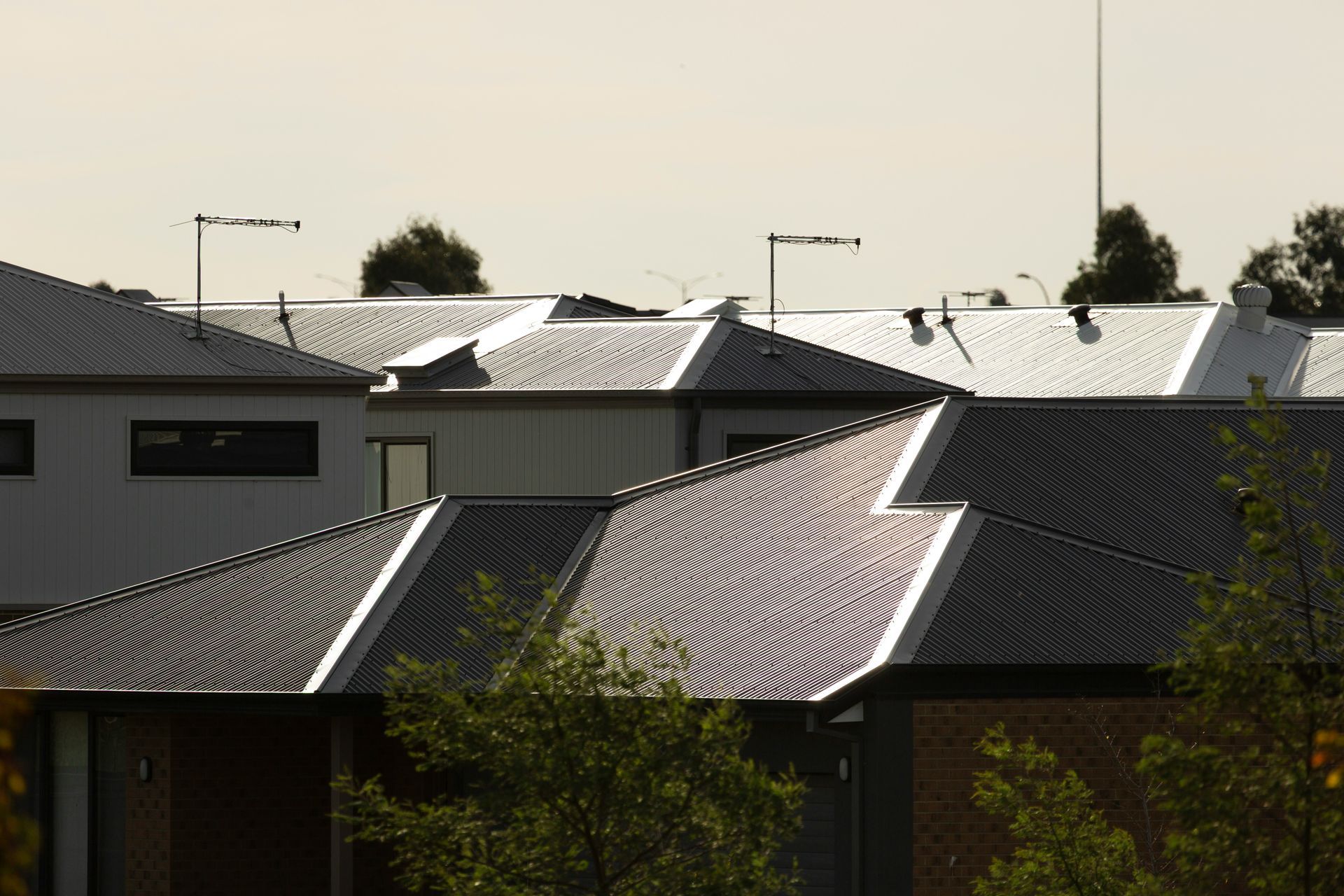 Rooftops With Sunlight Reflecting Off Metal Roofs In A Residential Neighborhood — Gibson Plumbing & Roofing Pty Ltd in Boyne Island, QLD