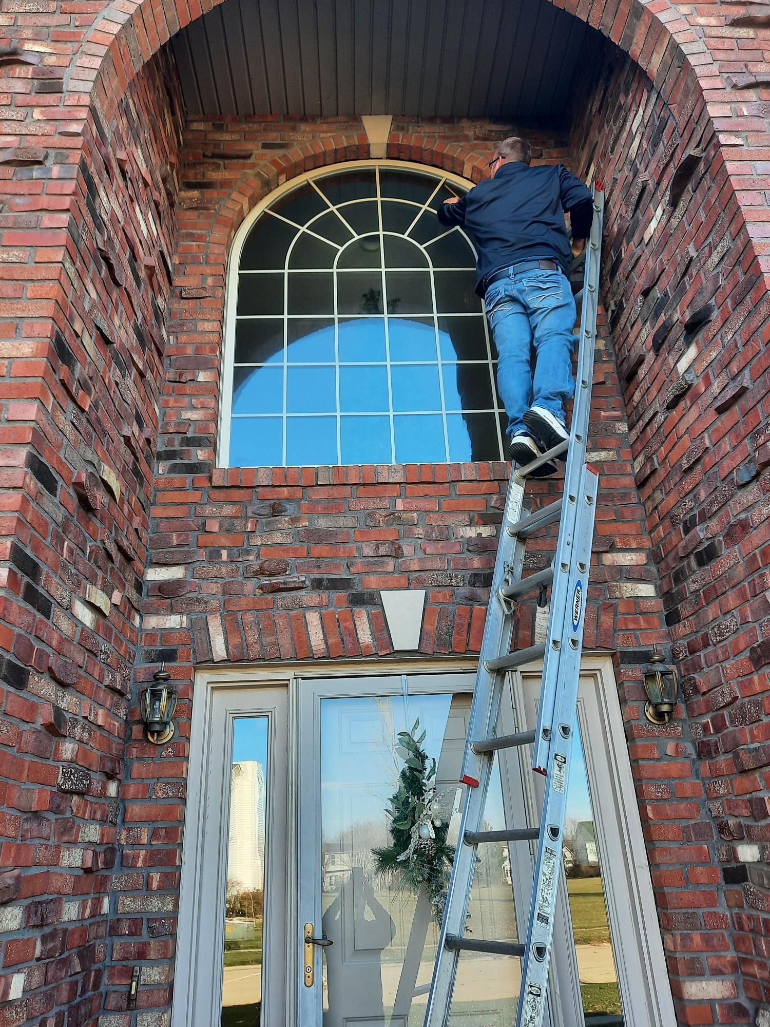 A man on a ladder cleaning the window of the building | Champaign, IL | Precision Maintenance