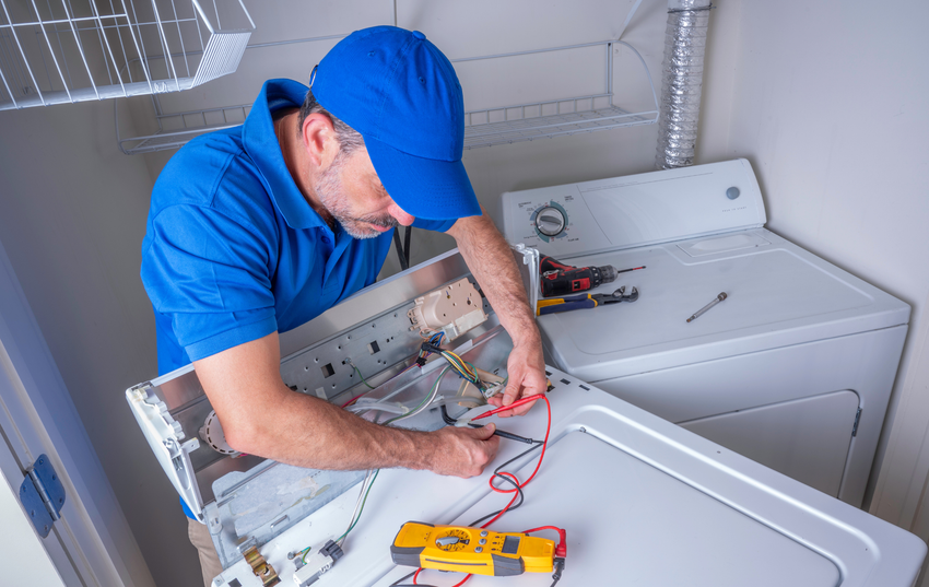 A man is fixing a washer and dryer in a laundry room.