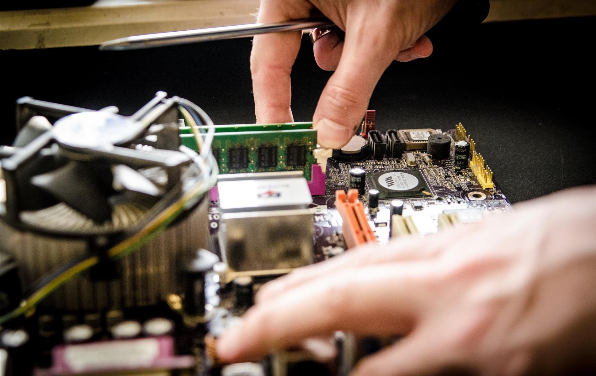 A person is working on a computer motherboard with a screwdriver.