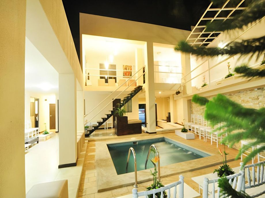 Un patio iluminado con una pequeña piscina, una escalera que conduce a un nivel superior y sillas blancas dispuestas para un evento.