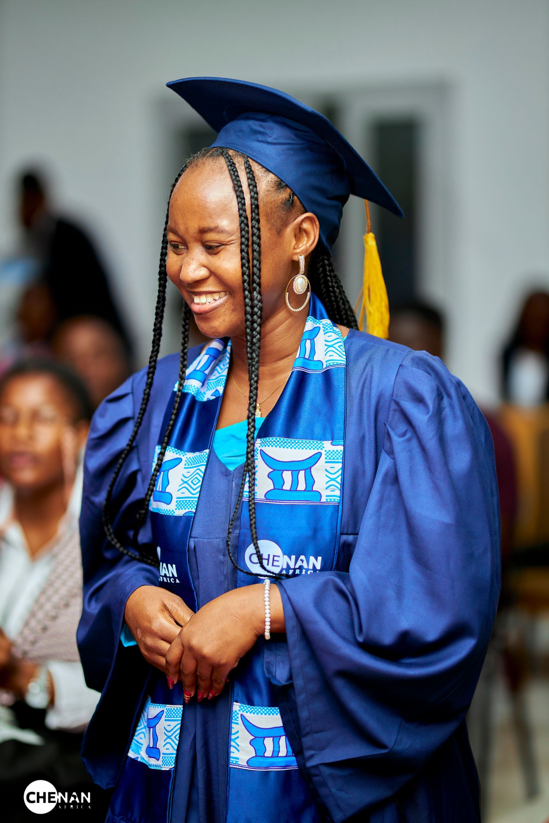 Une femme en robe de remise de diplôme bleue sourit, debout à l'intérieur.