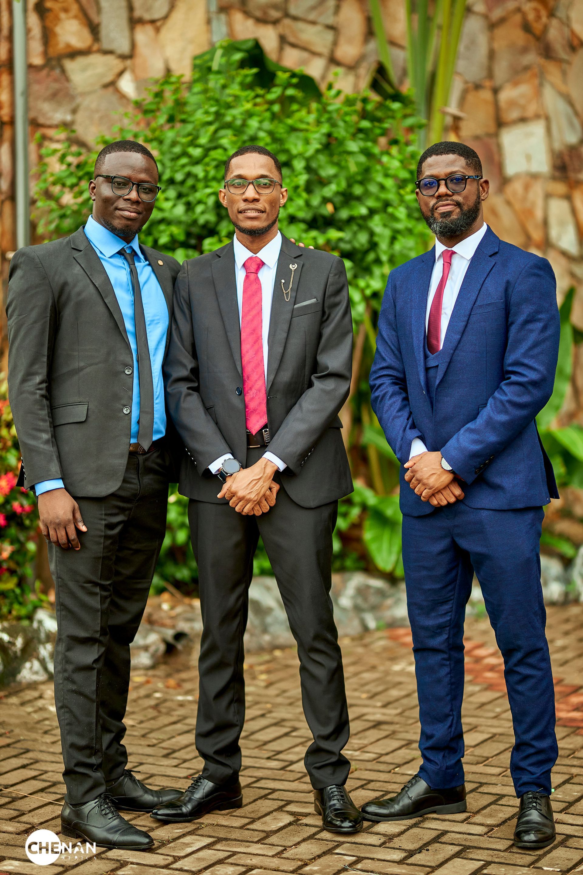 Trois hommes en costume posent à l'extérieur pour une photo.