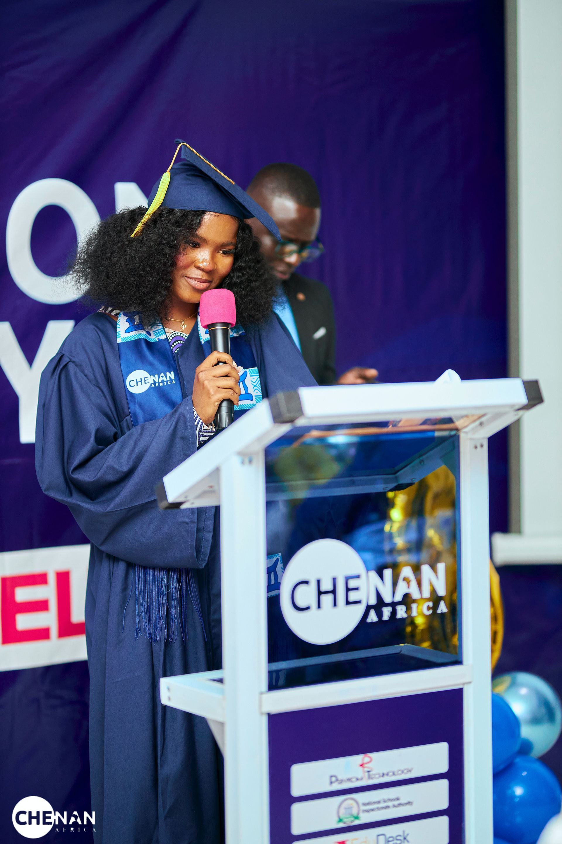 Une femme en robe de remise de diplôme prend la parole à la tribune, le logo « CHENAN AFRICA » est visible.