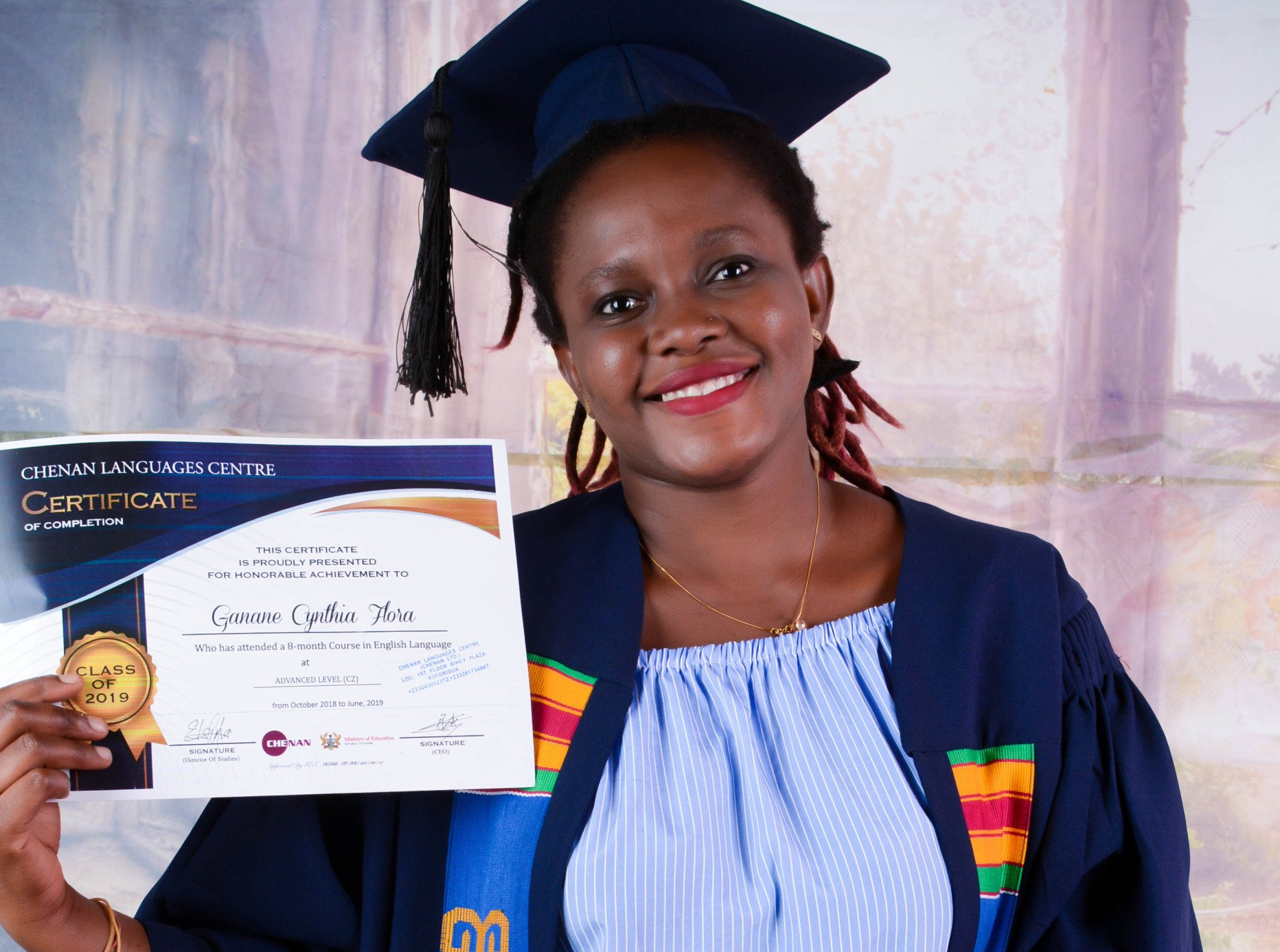 Femme en toque et robe de remise de diplôme, tenant son certificat, souriante.