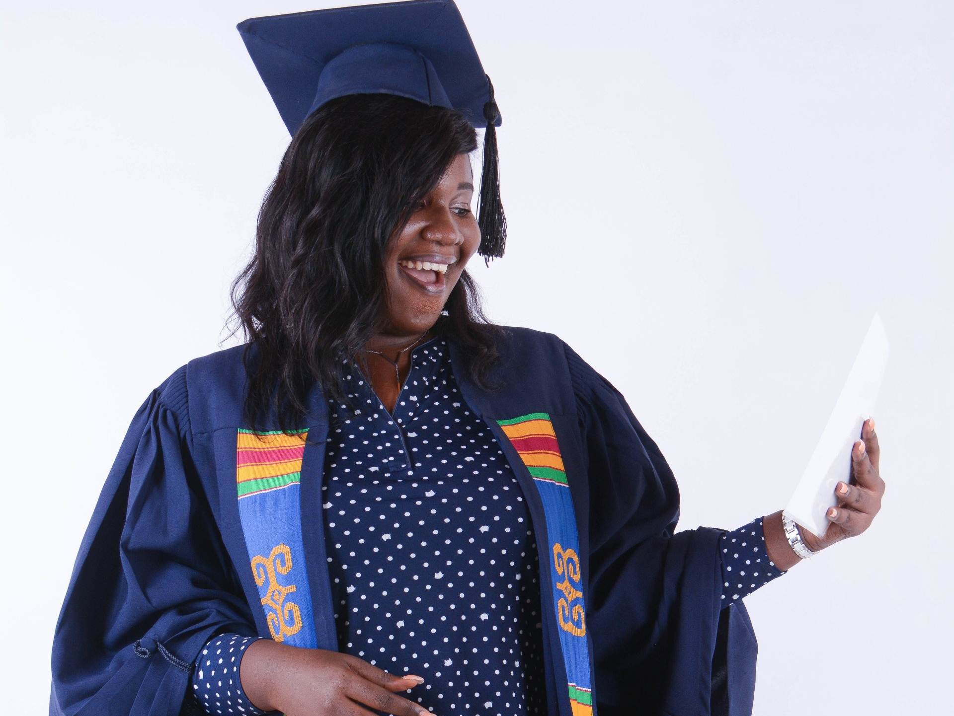 Femme en toge et toque de remise de diplôme, tenant son diplôme, souriant d'excitation.