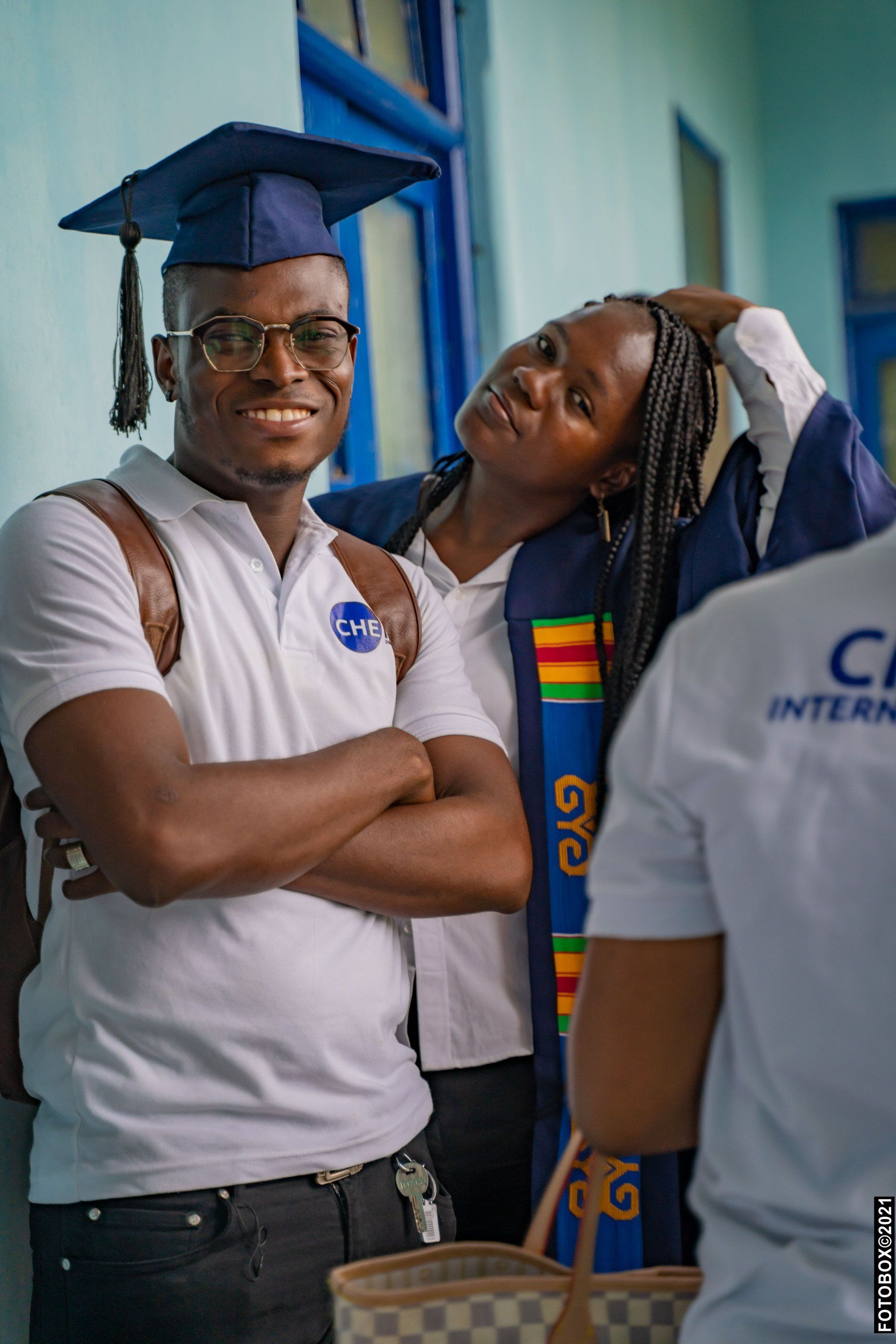 Un homme coiffé d'une toque de diplômé et une femme portant une étole de remise de diplôme posent en souriant dans un couloir.
