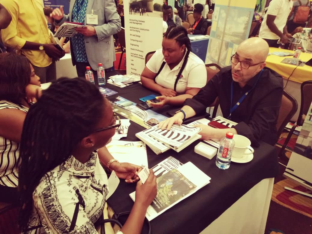 Des personnes assises à une table consultent des brochures. Plusieurs d'entre elles discutent. Événement en intérieur.