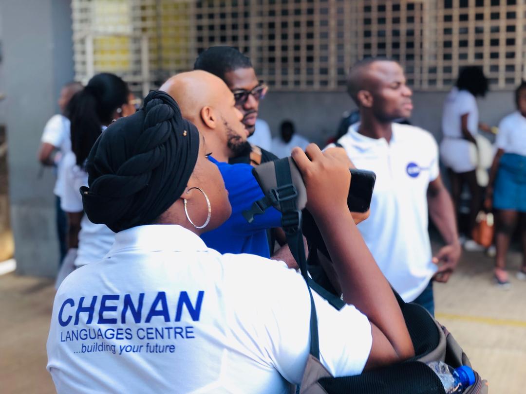 Des personnes vêtues de chemises blanches, dont une portant l'inscription « CHENAN LANGUAGES CENTRE », étaient rassemblées à l'extérieur.
