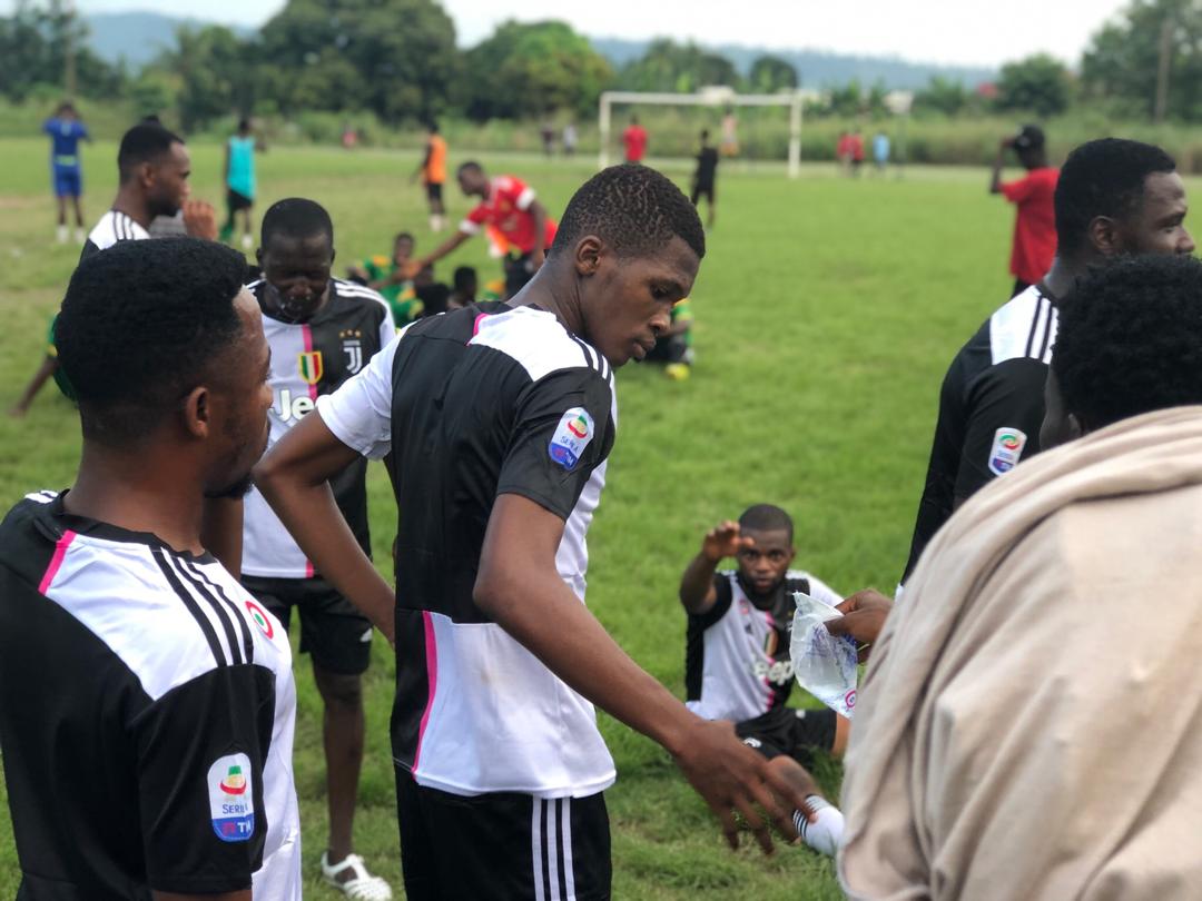 Des joueurs de football en maillots noirs et blancs évoluent sur un terrain. Certains interagissent, d'autres se tiennent à l'arrière-plan, près du but.