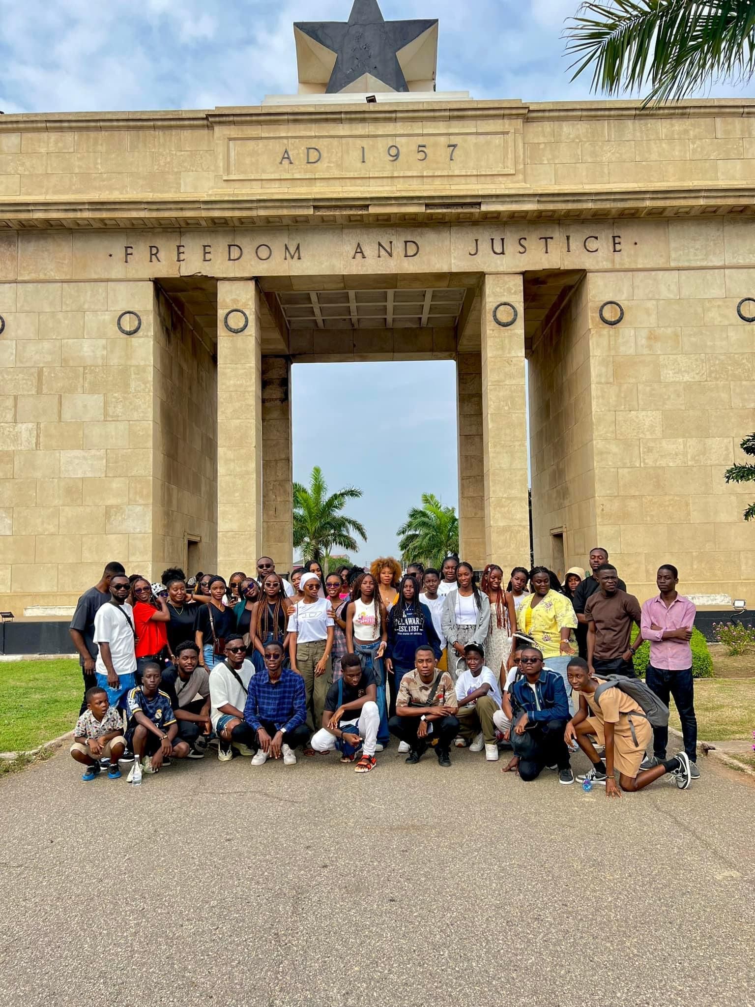 Groupe de personnes posant devant la Porte de l'Étoile Noire au Ghana, le texte indique « Liberté et Justice ».