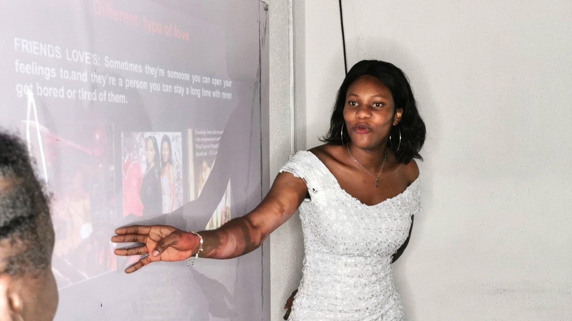 Une femme en robe blanche présente un écran affichant du texte et des images, en désignant du doigt un écran.