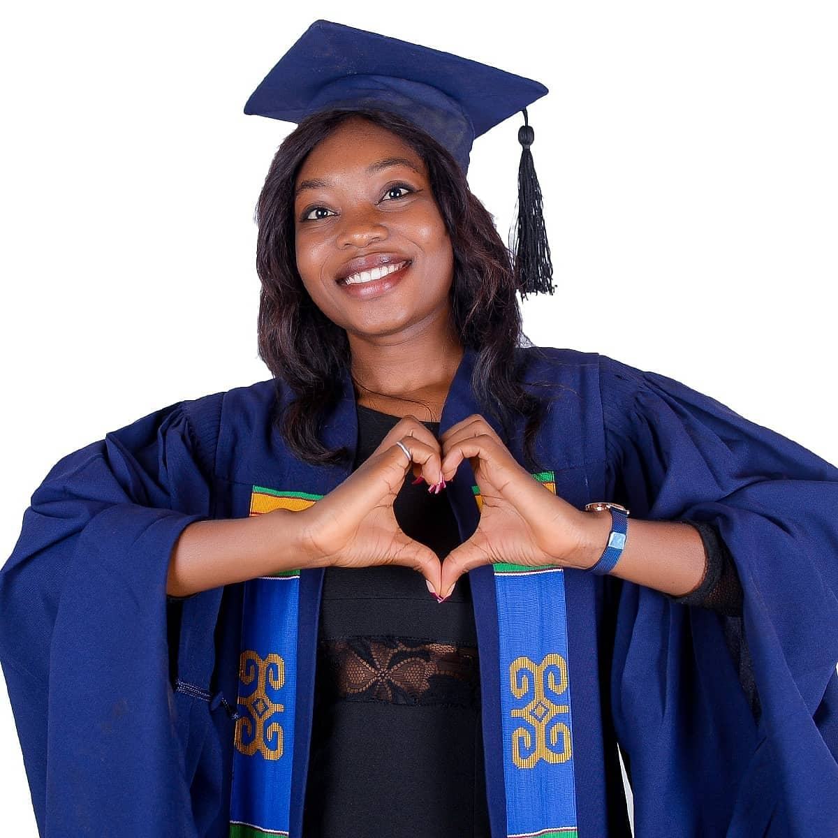 Une femme dans une casquette et une robe de graduation faisant une forme de coeur avec ses mains