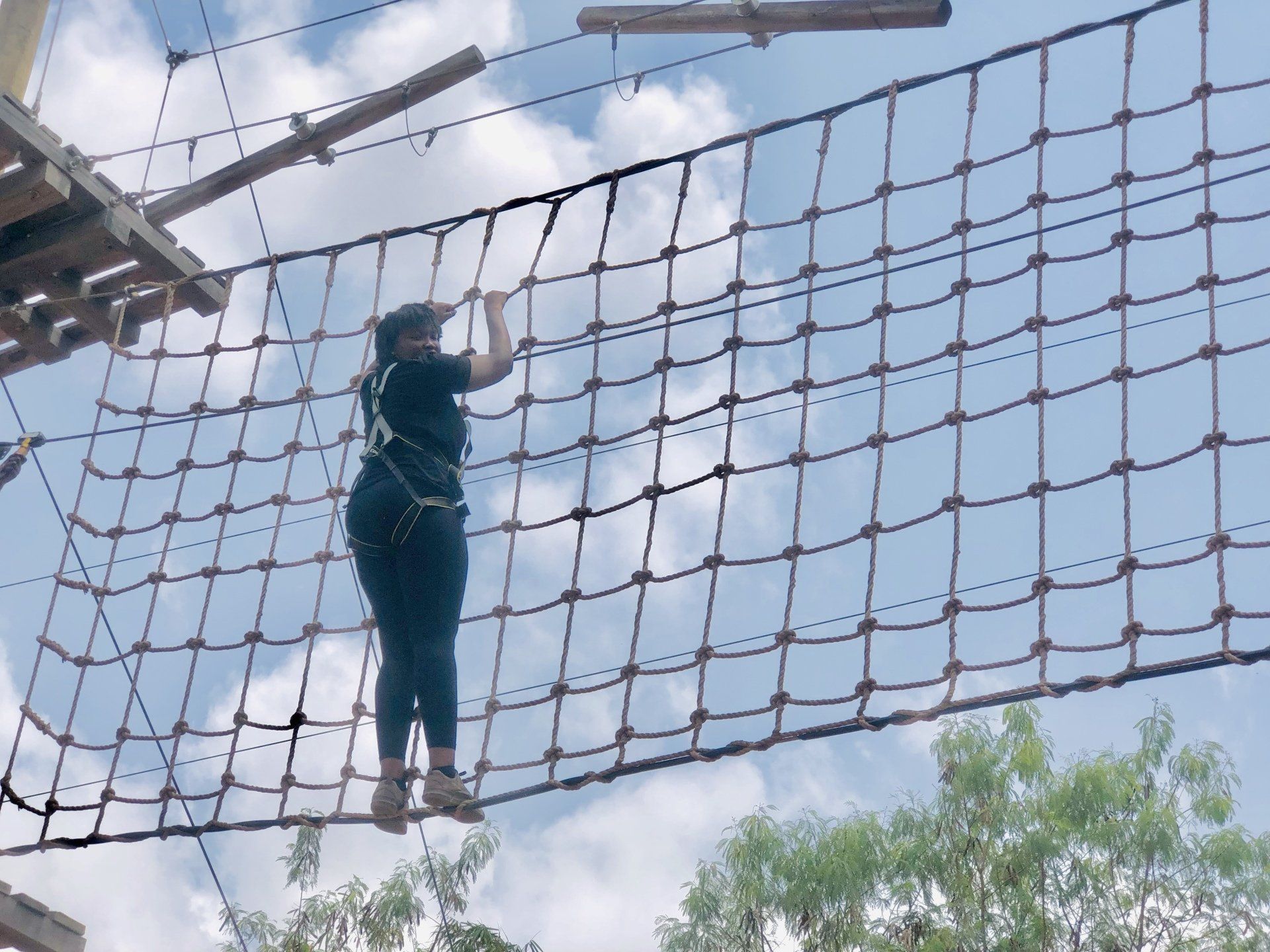 Une personne traverse un pont de corde dans un parc d'aventure en plein air par une journée ensoleillée.