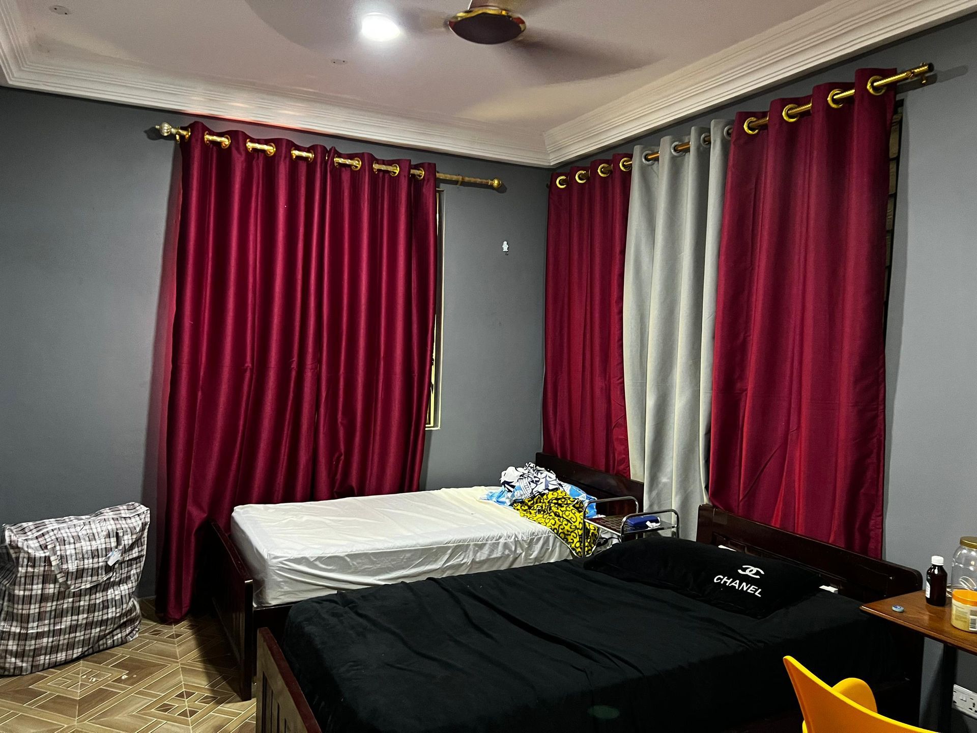 Chambre avec deux lits, rideaux rouges et murs gris.
