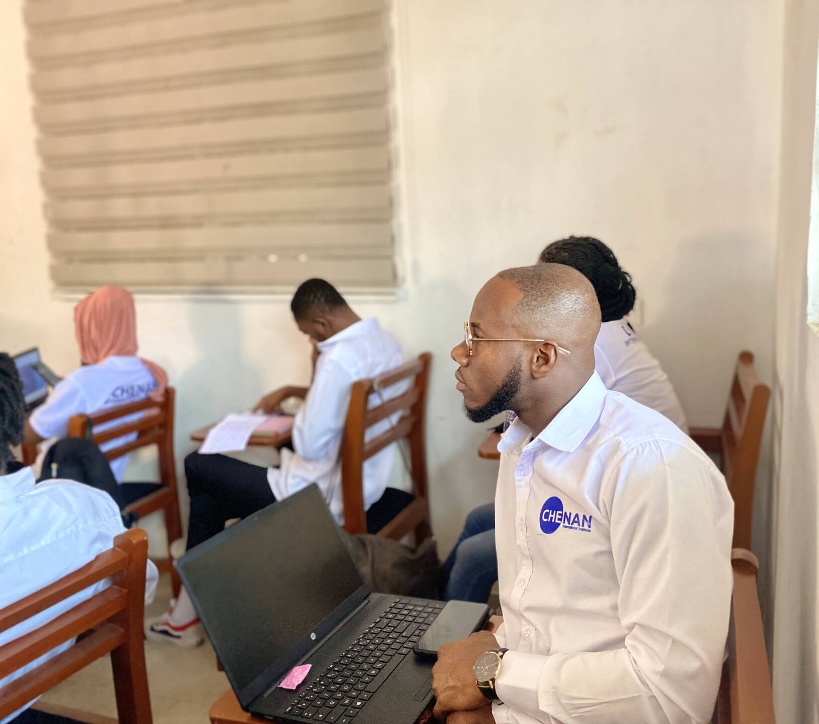 Un groupe d'apprenants de Chenan Africa est assis dans une pièce avec un homme assis devant un ordinateur portable