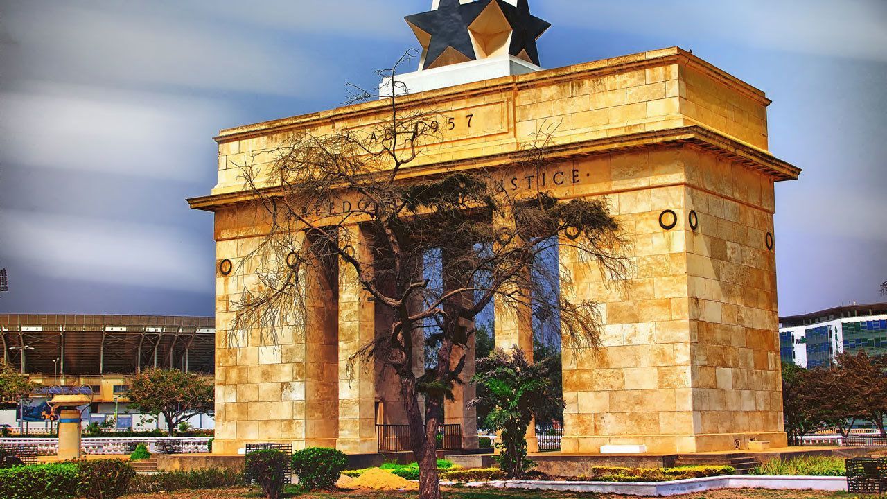La Porte de l'Étoile Noire à Accra, au Ghana, une grande arche de pierre surmontée d'une étoile noire, des arbres au premier plan, ciel nuageux.