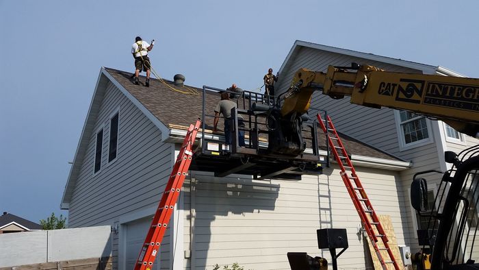 Roofers in the Fargo-Moorhead area wearing safety harnesses tearing off dimensional shingles into dumpster starting with ridge cap