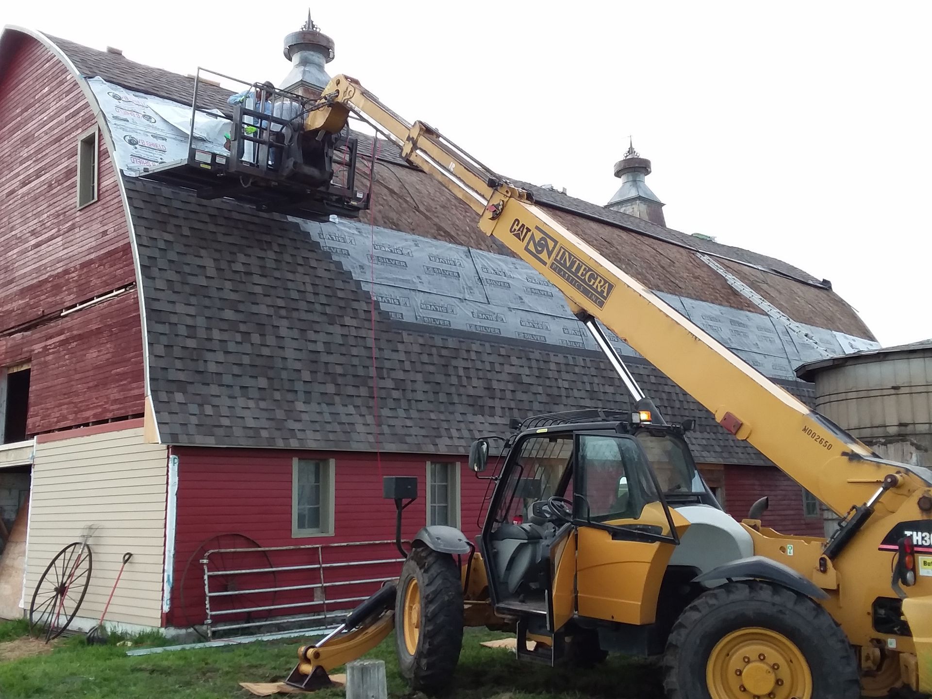 Laminate Shingles being installed on a curved barn roof using a Telehandler near Fargo-Moorhead