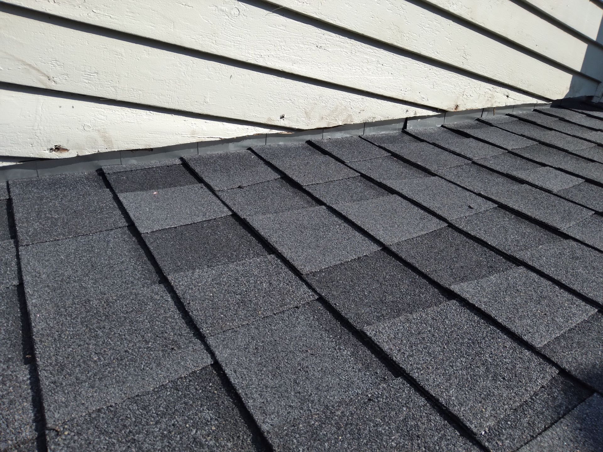 Moire Black architectural shingles interweaved with new roof step flashing behind wood siding in Hillsboro, North Dakota