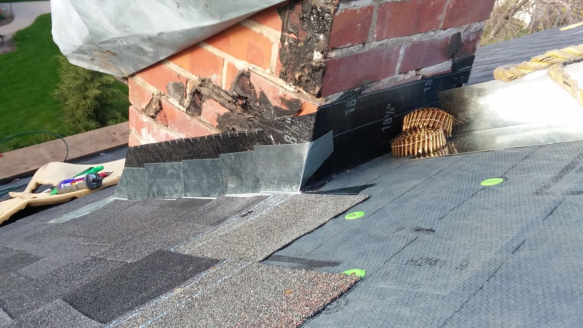 Detroit Lakes roofer installing metal step flashing on brick chimney with extra coils of roofing nails resting above chimney