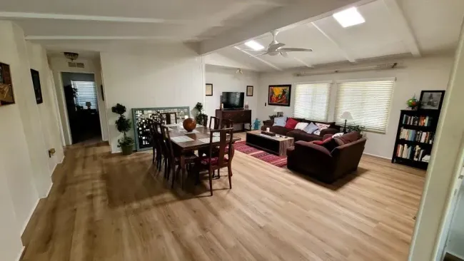 An open-concept living and dining room with wood-look flooring, a dining table, a dark sofa, and a bookshelf.