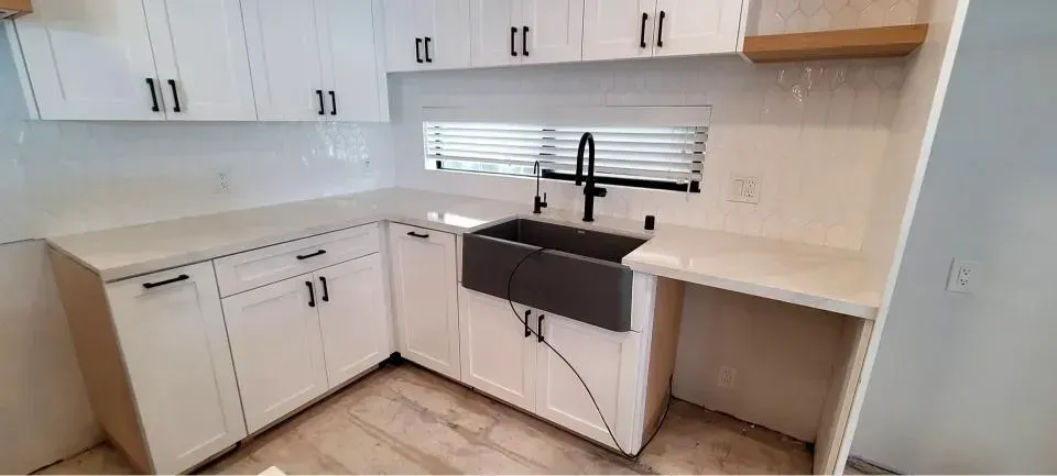 A kitchen with white cabinets, a dark farmhouse sink, a black faucet, and a light-colored countertop.