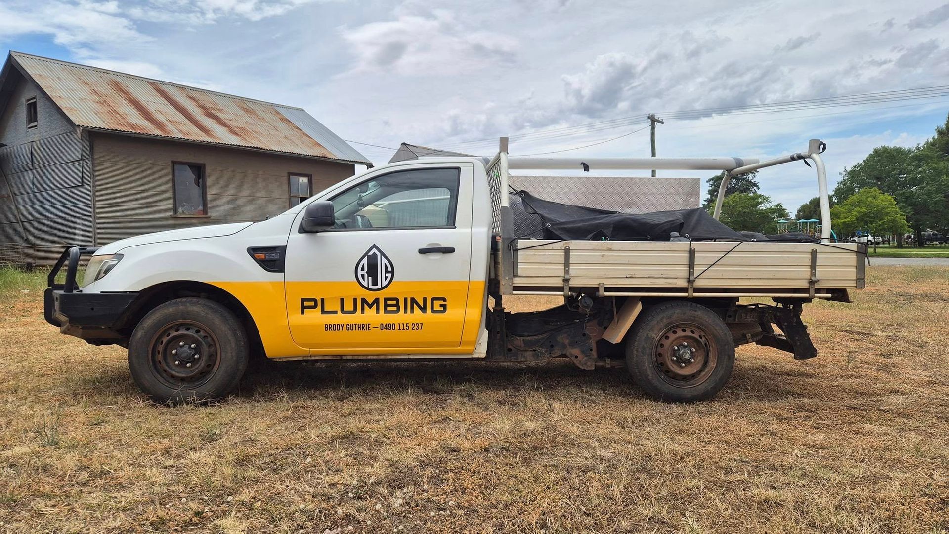 White and yellow plumbing service truck parked in a grassy field under a cloudy sky — BJG Plumbing in Coolamon, NSW