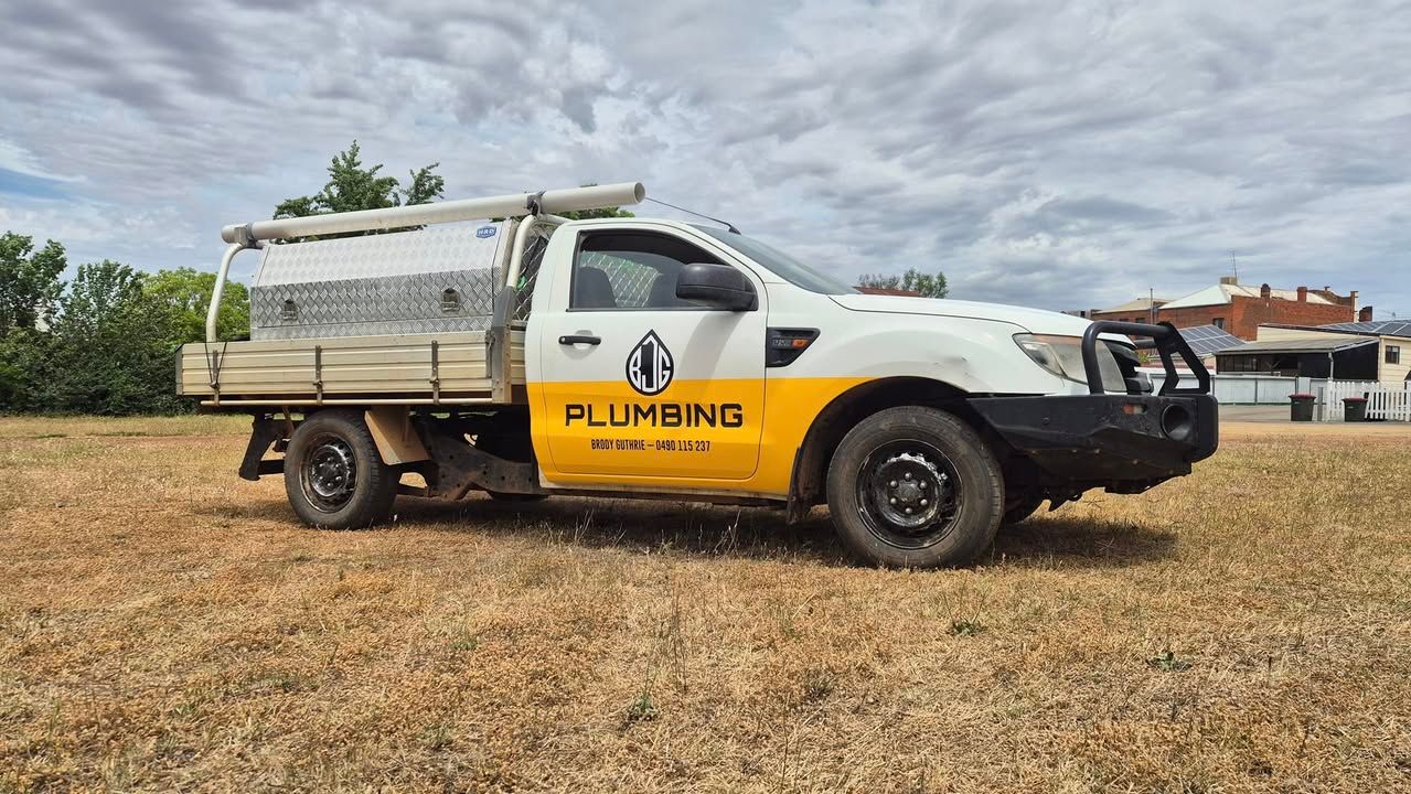White and yellow plumbing truck parked on dry grass, cloudy sky backdrop — BJG Plumbing in Coolamon, NSW