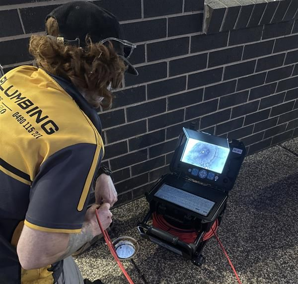 Plumber using a camera to inspect a drainpipe near a brick wall — BJG Plumbing in Coolamon, NSW