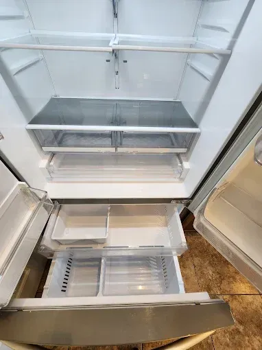 Inside view of an empty stainless steel refrigerator with multiple clear plastic shelves and drawers.