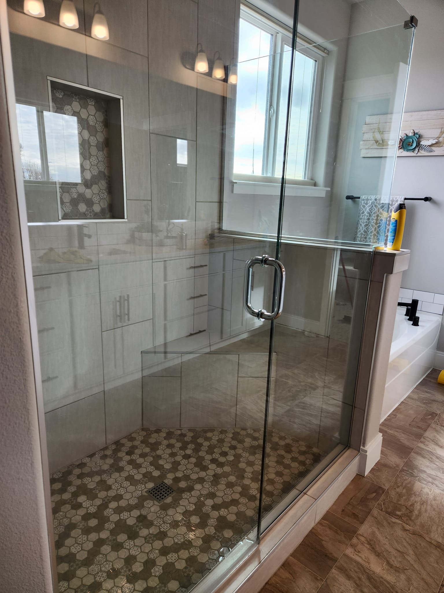 A bathroom featuring a glass-enclosed shower with pebble-tile flooring, next to a vanity with a mirror and a bathtub.