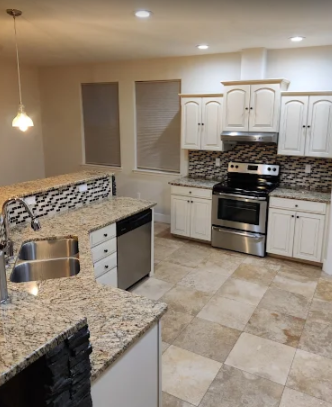 A kitchen with granite countertops, light cabinets, stainless steel appliances, and a tiled backsplash and floor.