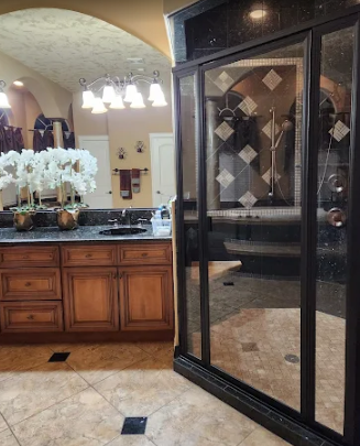 A bathroom featuring a dark wood vanity with a black countertop and a large walk-in shower with dark trim.